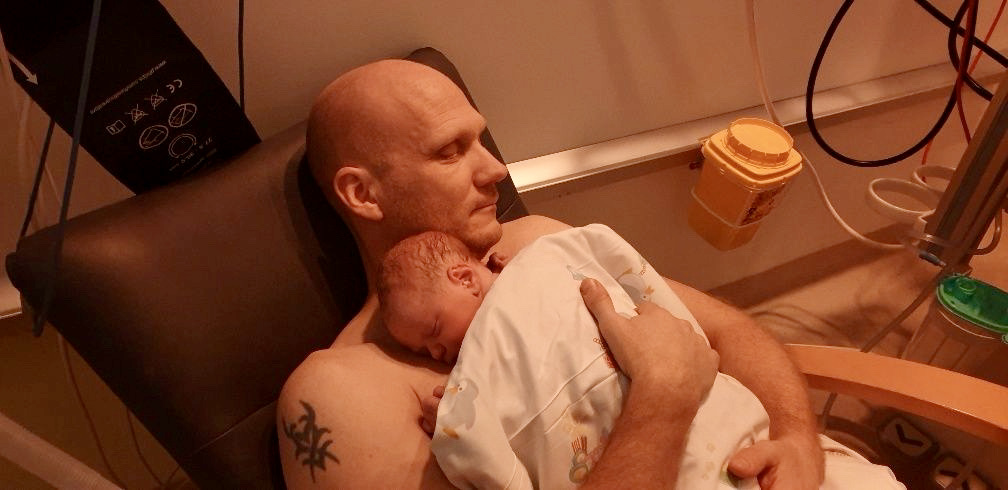 Partneren sidder hud mod hud med det nyfødte barn